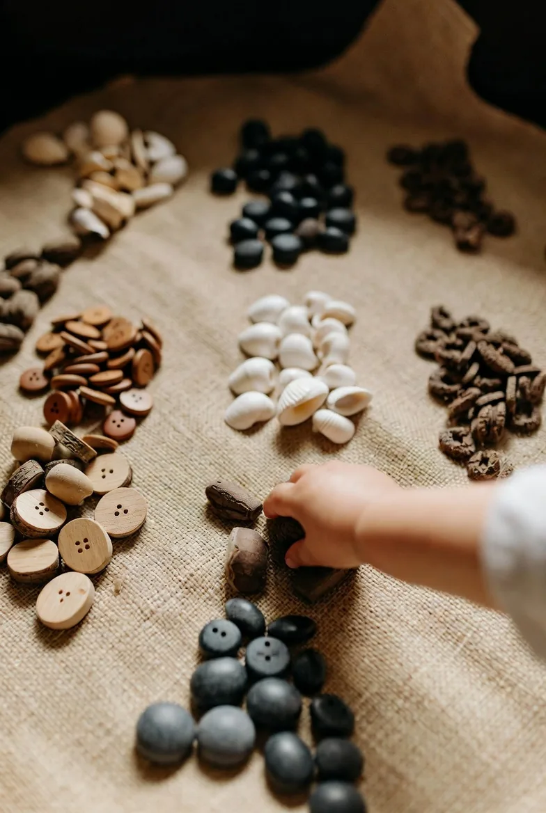A child sorting buttons and seeds into groups on cloth